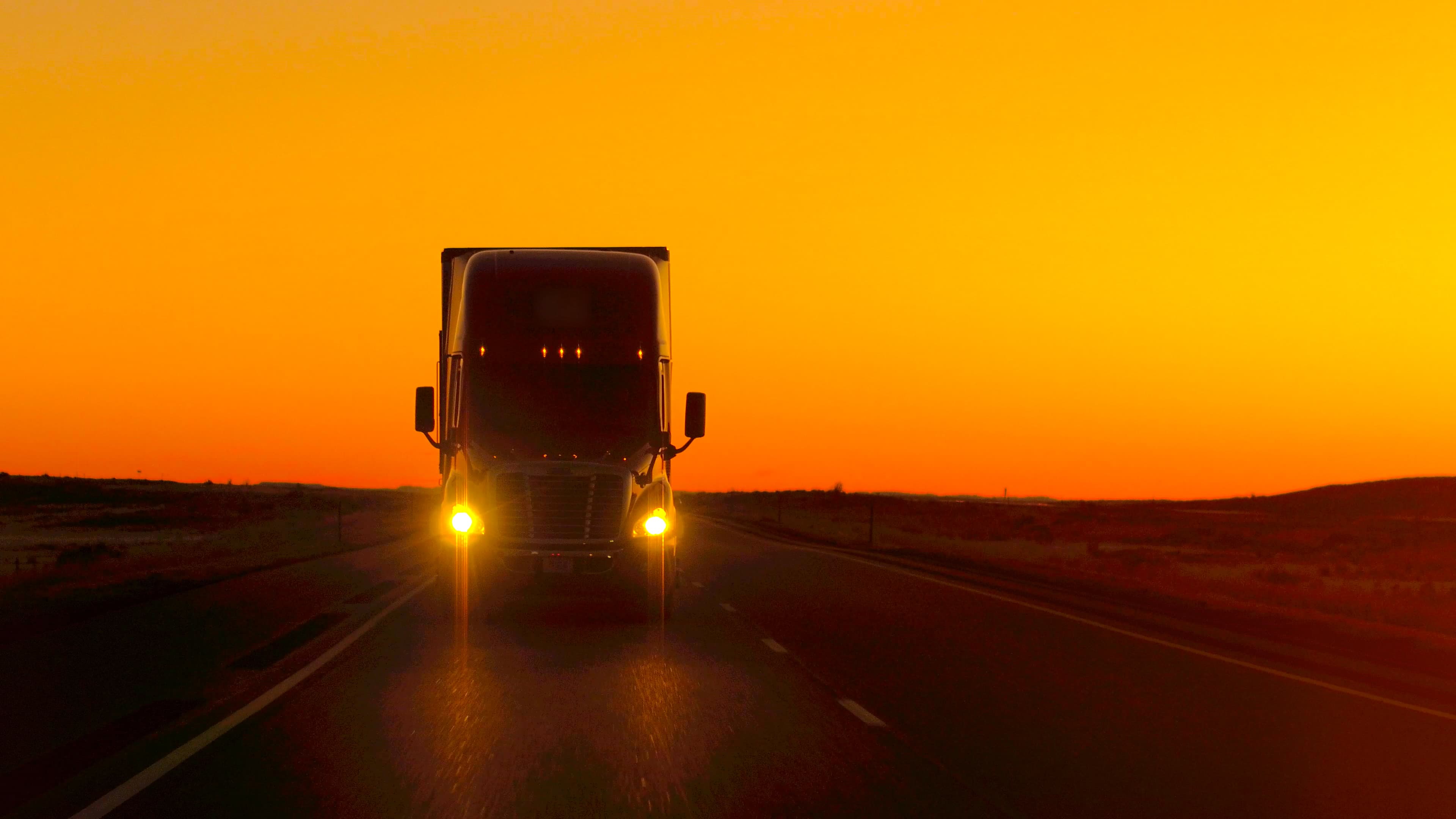 Semi-truck on an open highway at sunrise